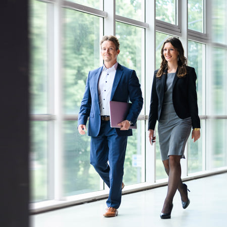 Zwei Menschen im Business Look  laufen einen Gang entlang.