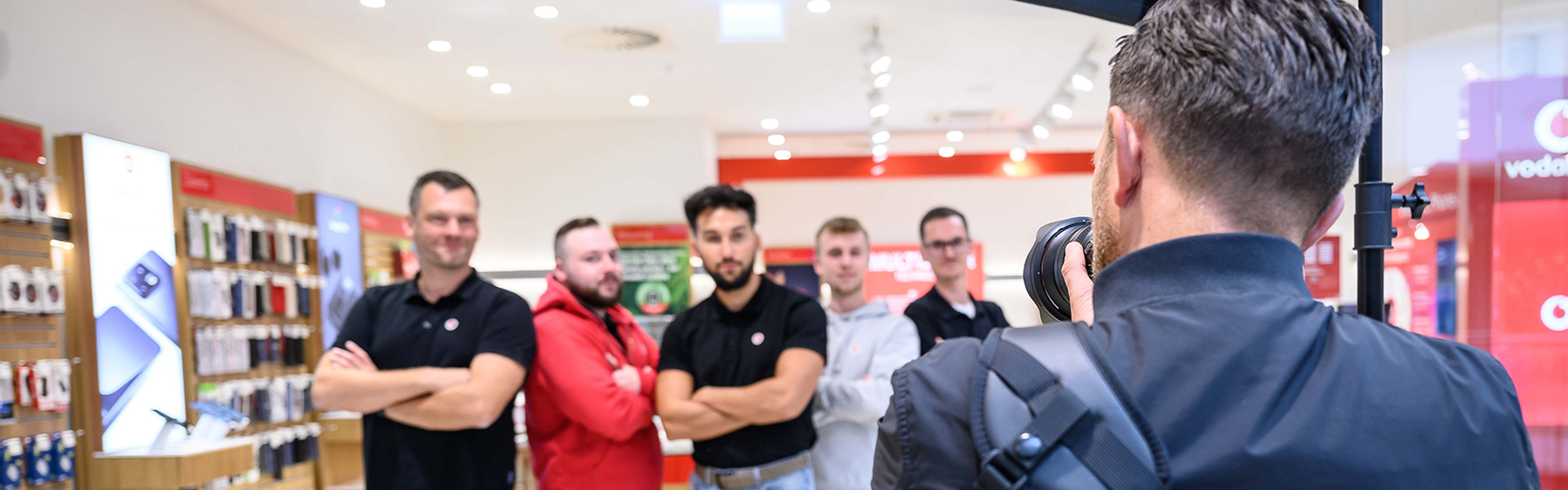 Ein männlicher Fotograf steht mit dem Rücken zum Betrachter und fotografiert eine Gruppe von Mitarbeitenden von Vodafone.